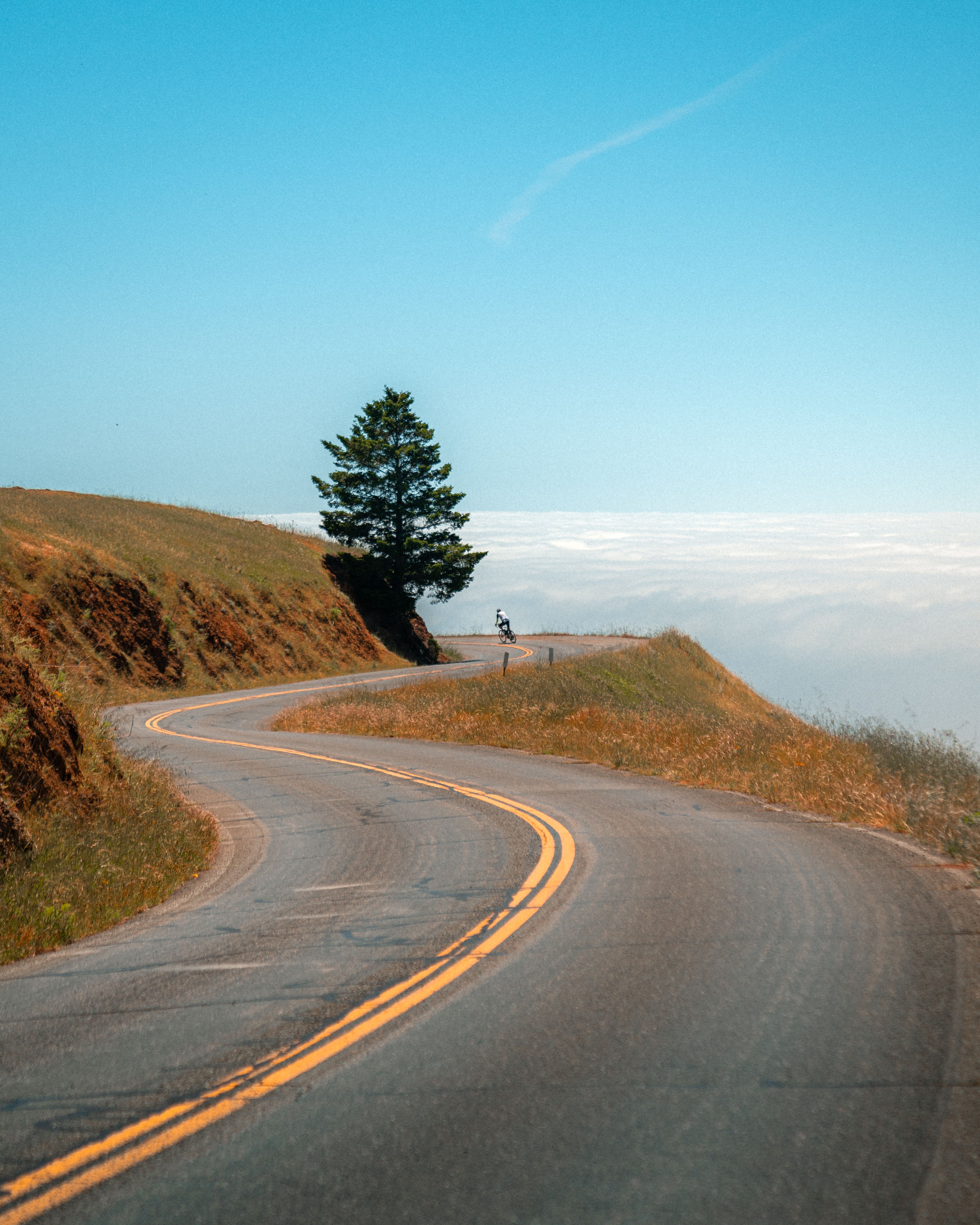A cyclist riding a winding coastal road above the clouds
