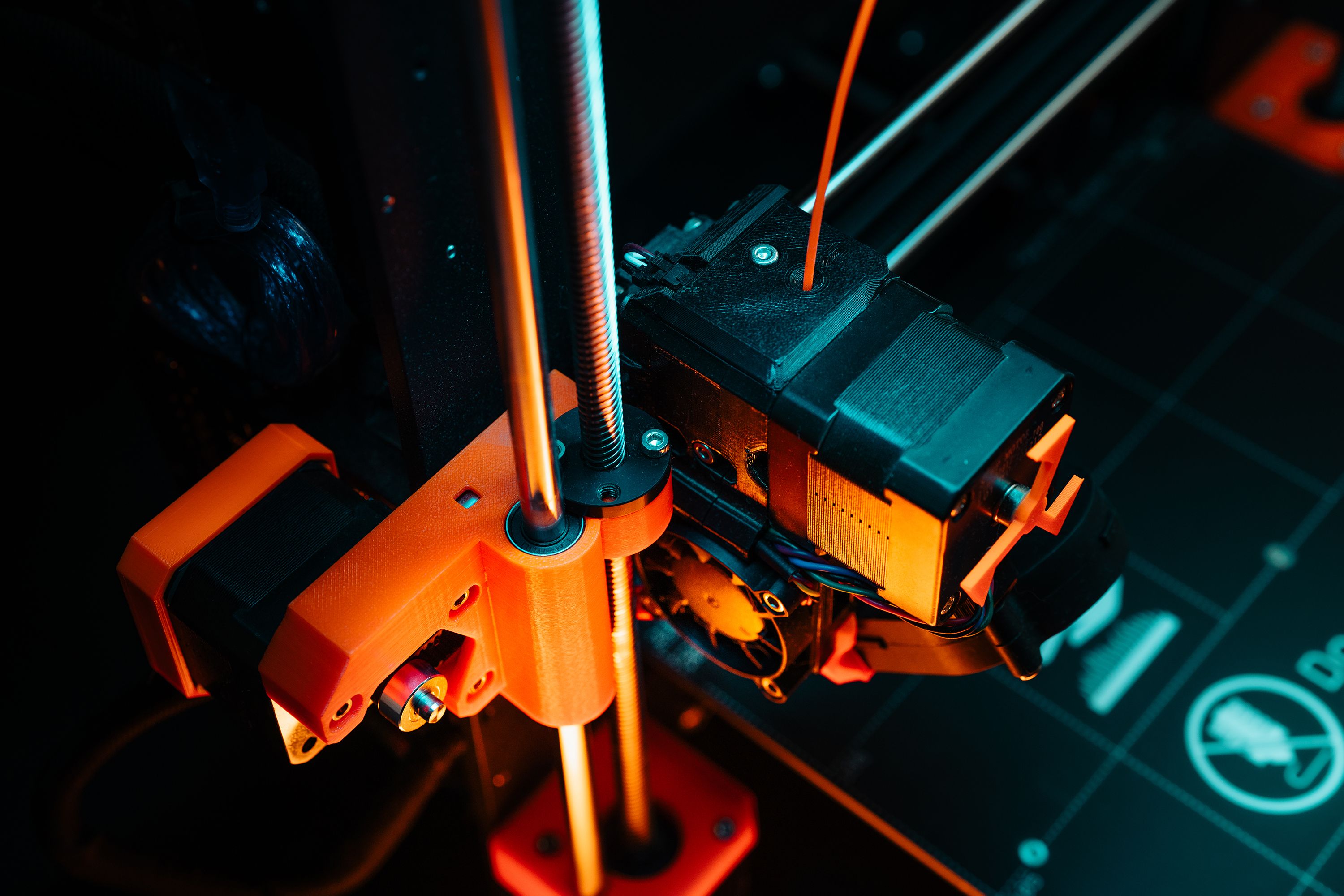 A close-up of a 3D printer mechanism with orange and teal light